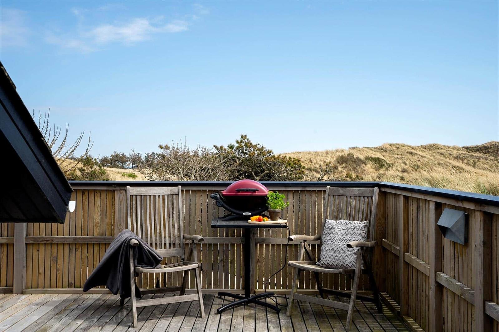 Terrasse mit Grill, zwei Stühlen und Blick auf Dünen.