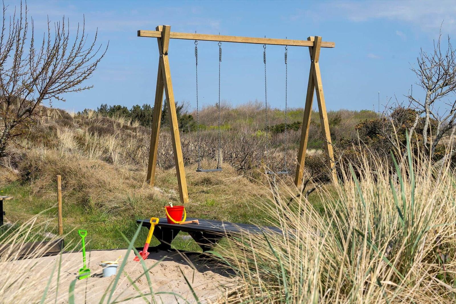Holzschaukel mit Kette und Sandkasten im Gras