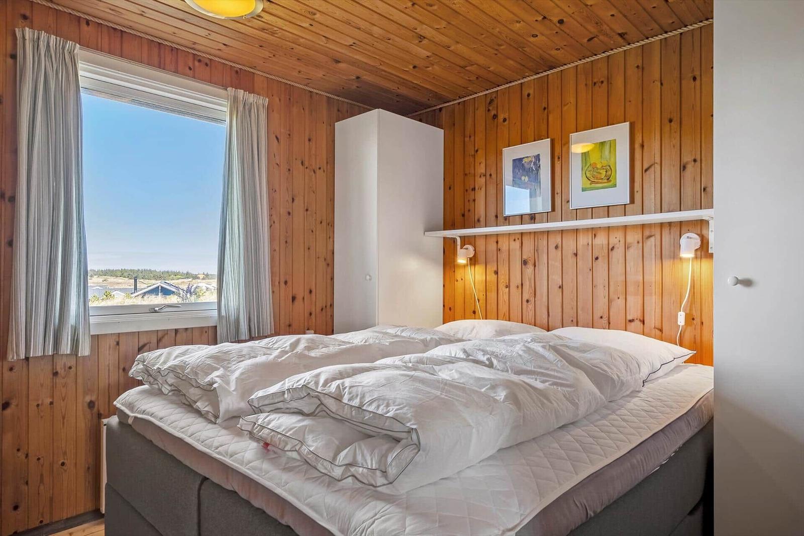 Schlafzimmer mit Holzwand, Bett und Fenster mit Blick.