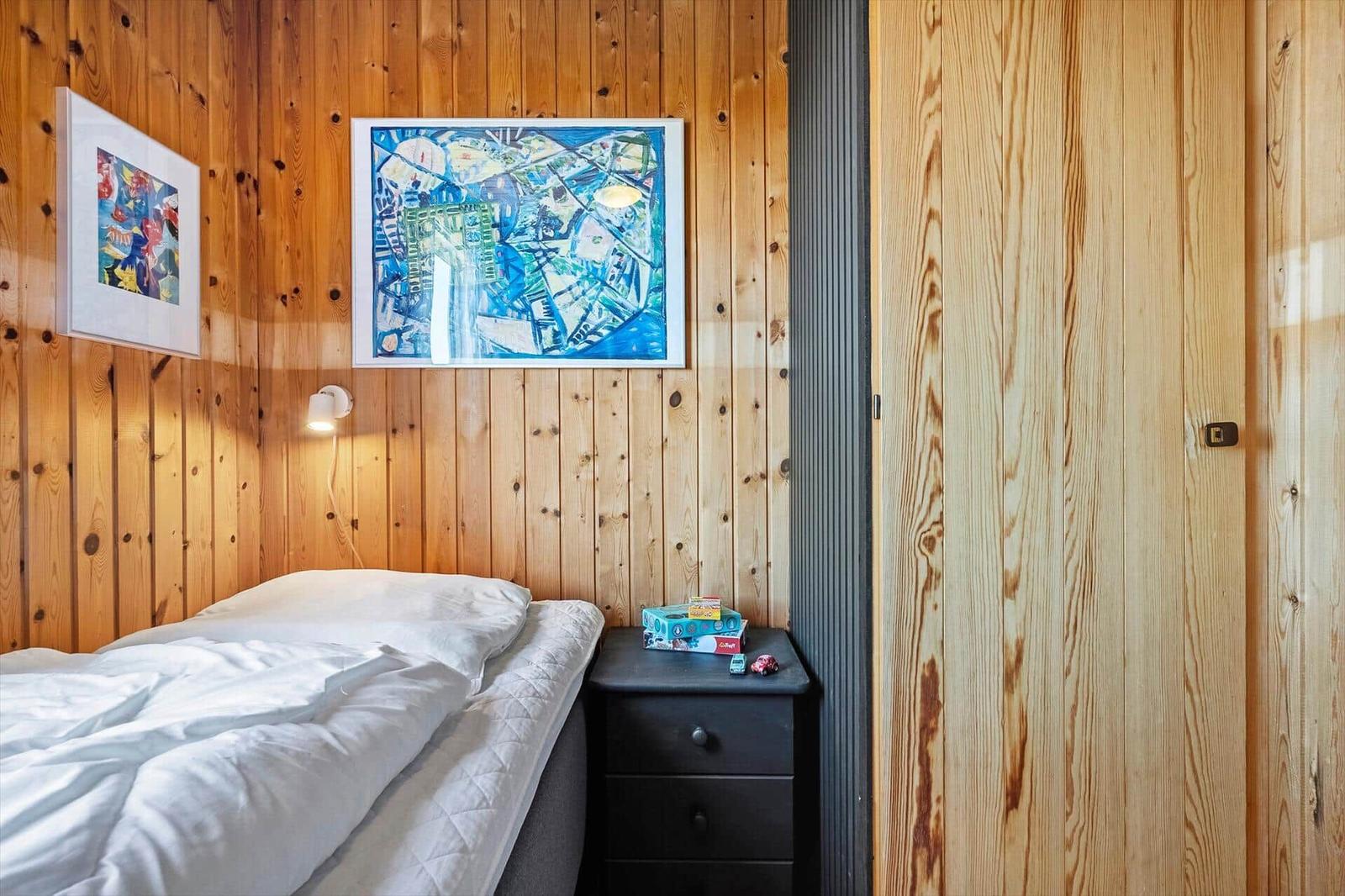 Schlafzimmer mit Holzwand, Bett, Nachttisch und Bildern an der Wand.