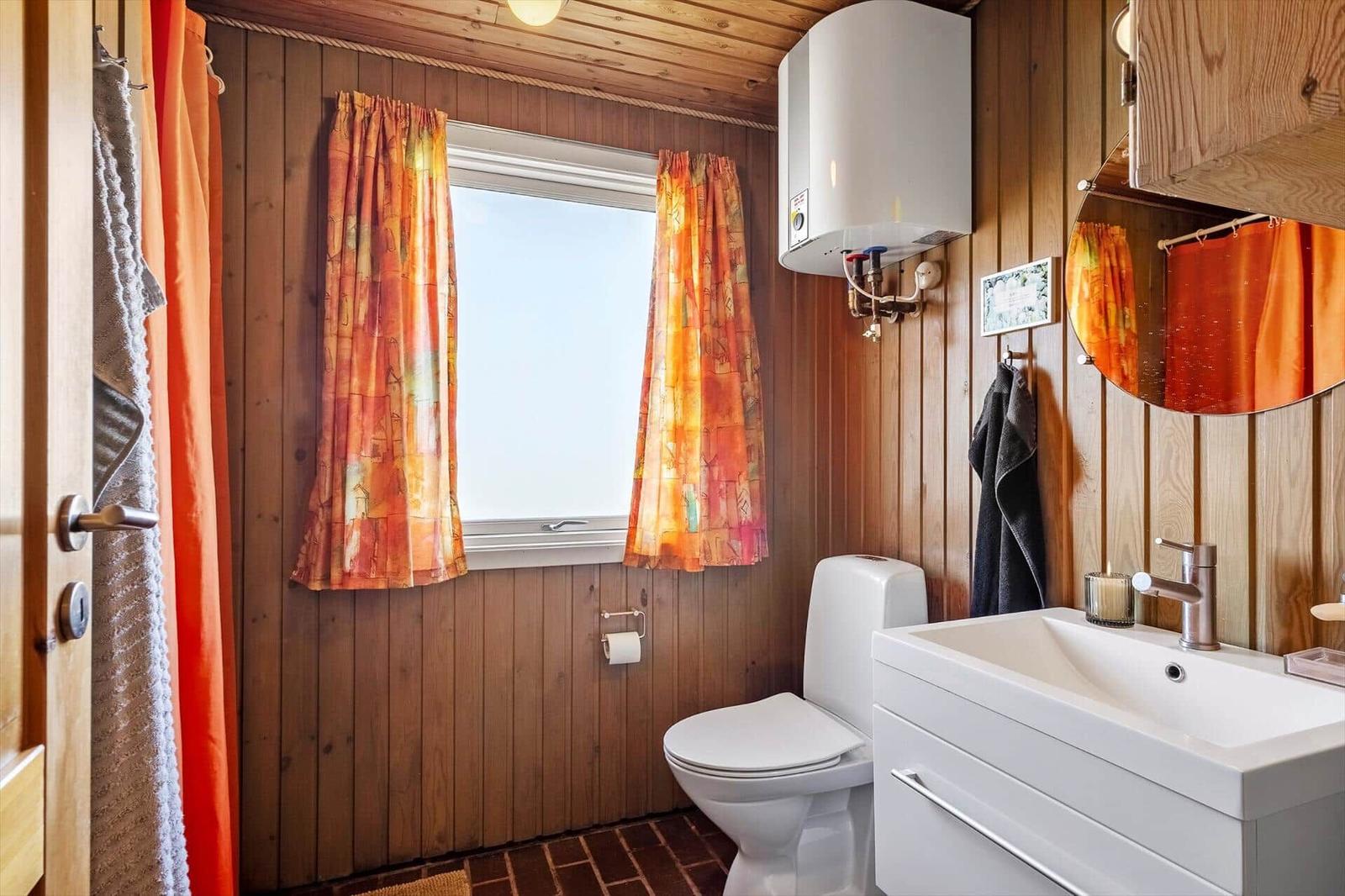 Badezimmer mit Holzwand, Fenster, WC und Waschbecken.