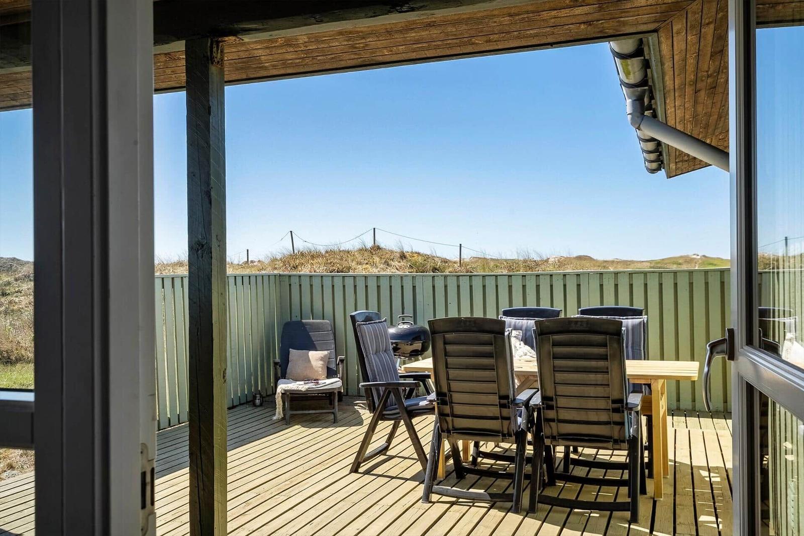 Terrasse mit Sitzgruppe, Grill und Blick auf Dünen.