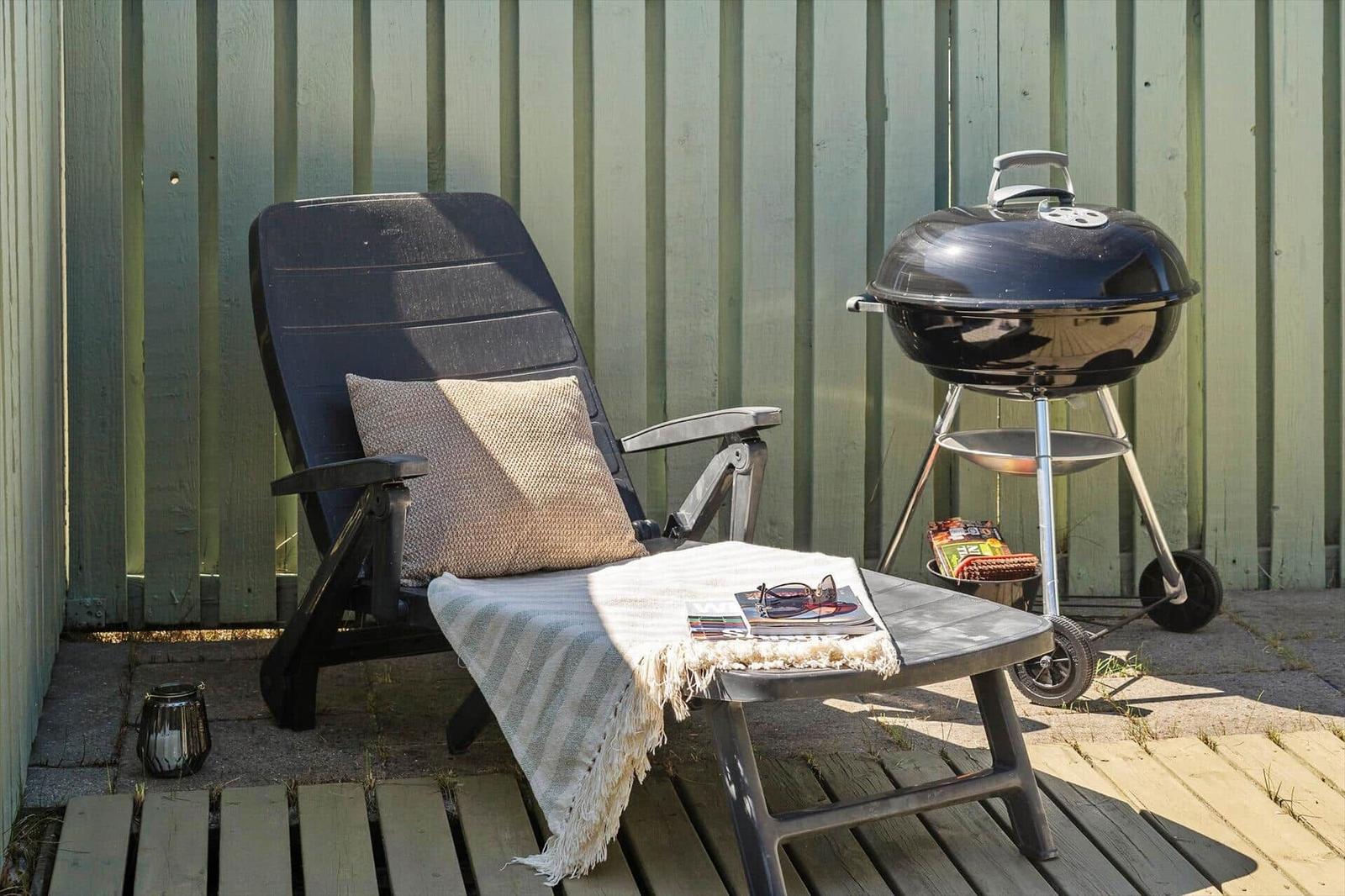 Schwarze Liegestuhl mit Kissen und Decke neben Grill auf Terrasse.