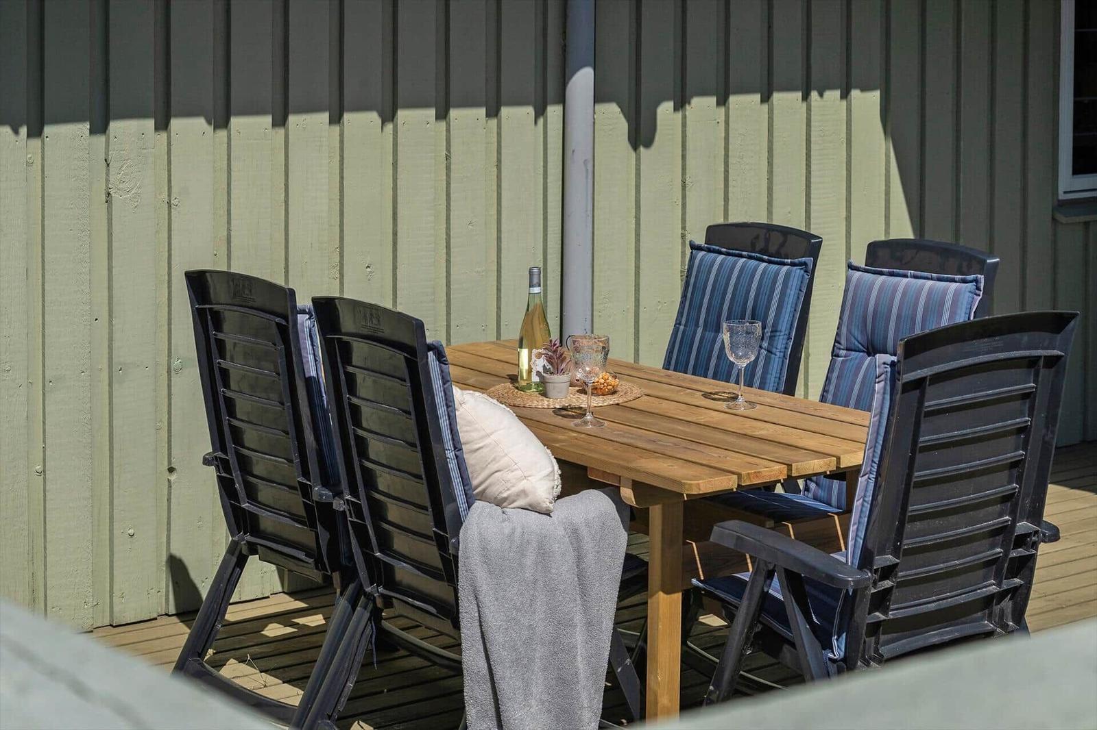 Holztisch mit Stühlen und Getränken auf einer Terrasse vor einem Haus.