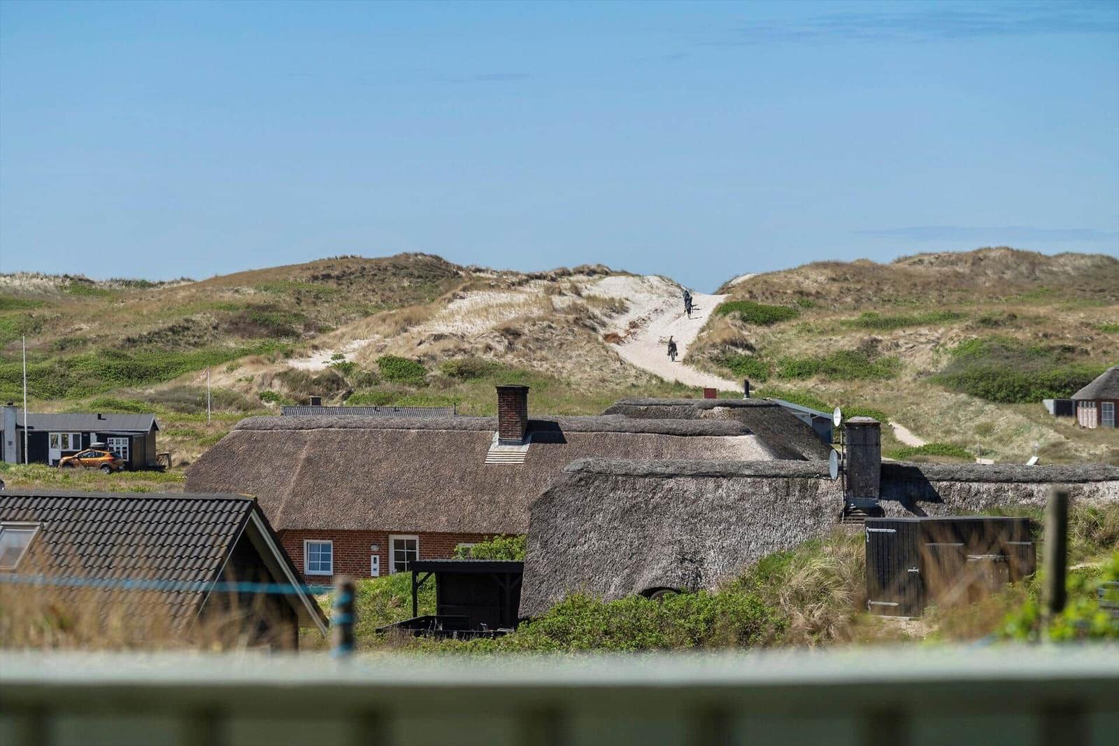 Dorf mit strohgedeckten Häusern und Dünen im Hintergrund.