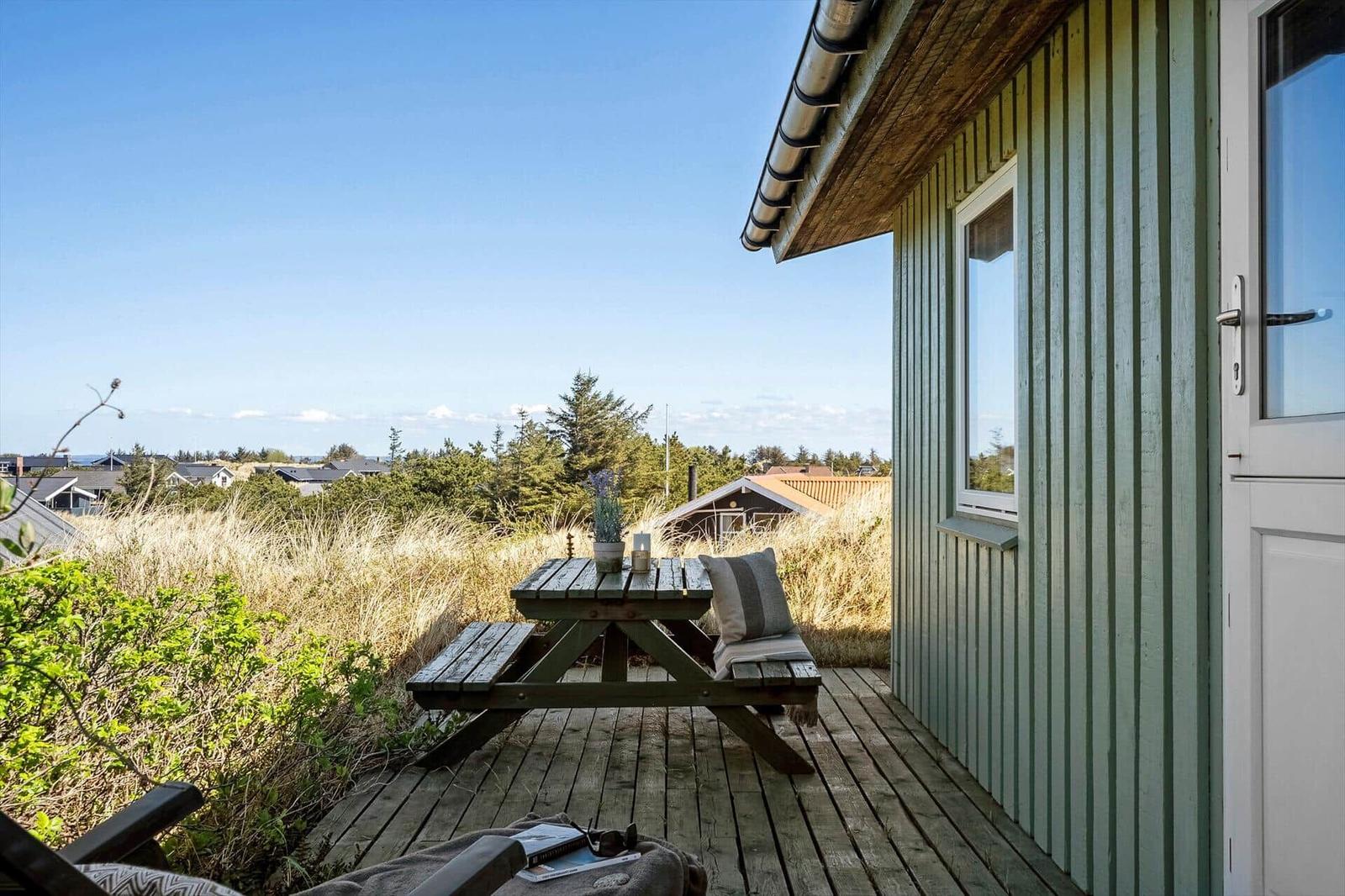 Terrasse mit Holztisch und Blick auf Grasland und Bäume.