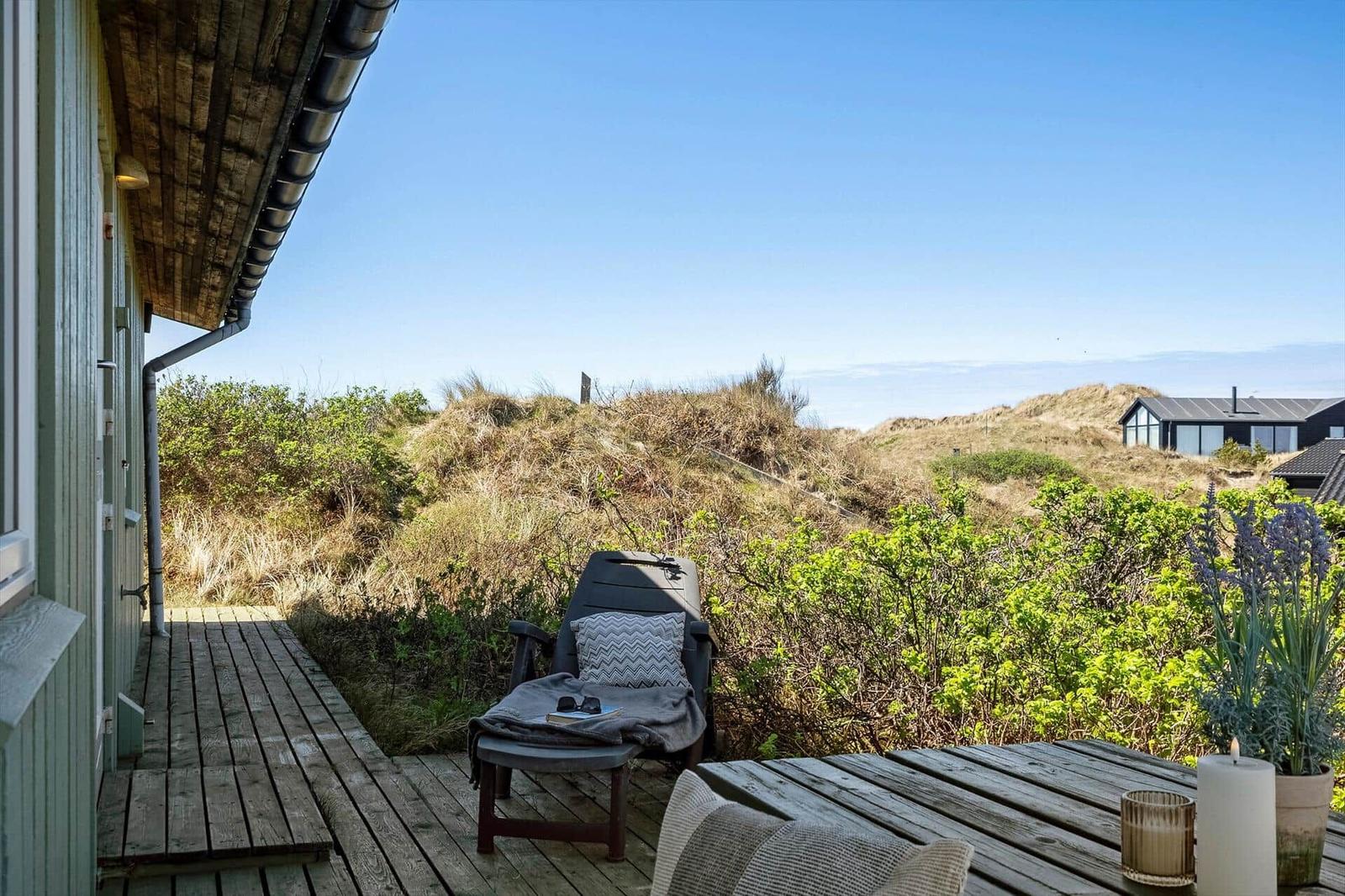 Terrasse mit Liegestuhl und Tisch. Blick auf Dünen und Ferienhaus im Hintergrund.