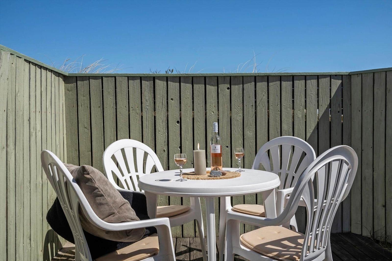 Rundtisch mit vier Stühlen auf Terrasse, Flasche Rosé und Kerze.