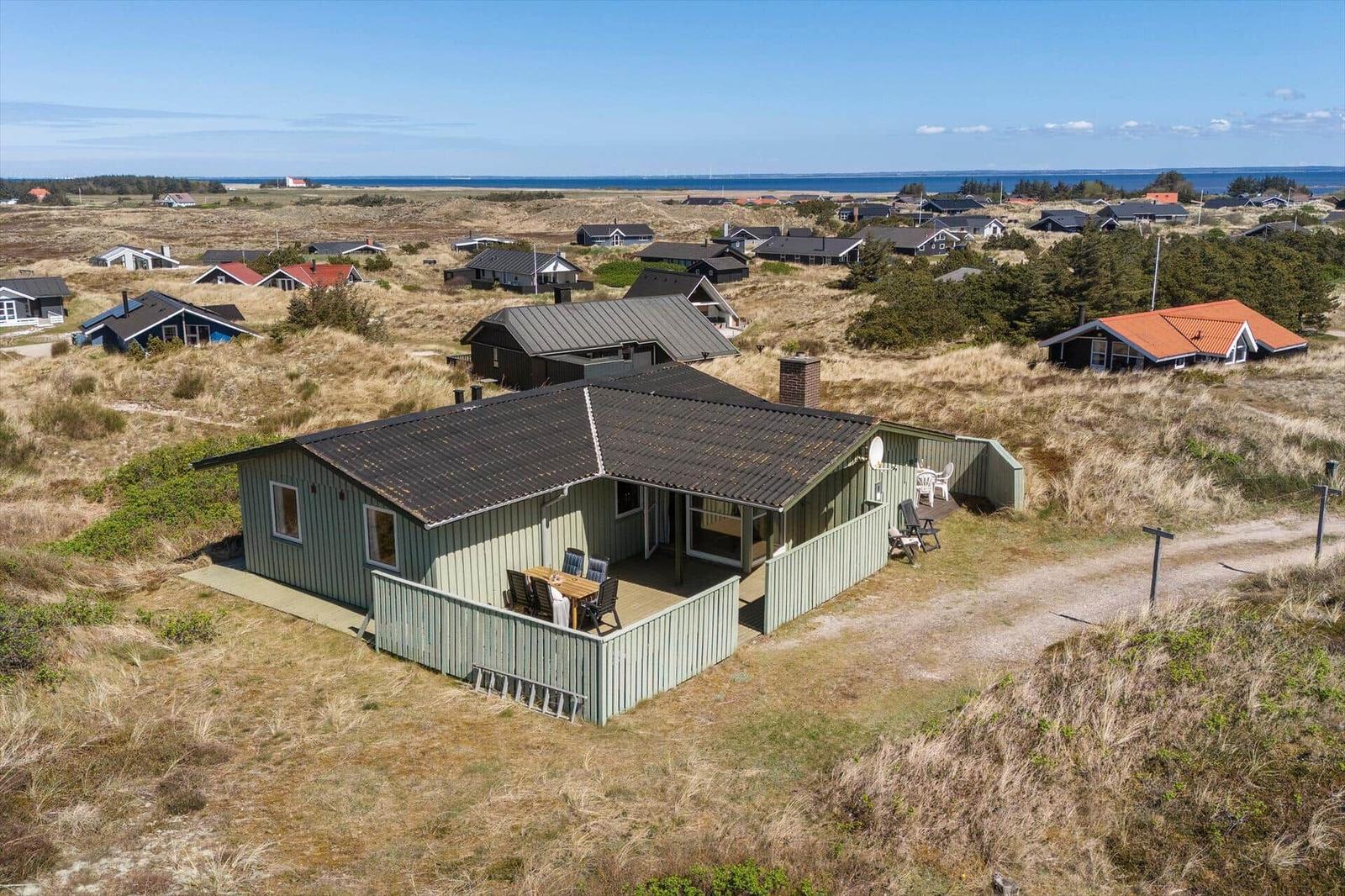 Ein Ferienhaus mit Terrasse und Meerblick in einer Dünenlandschaft.