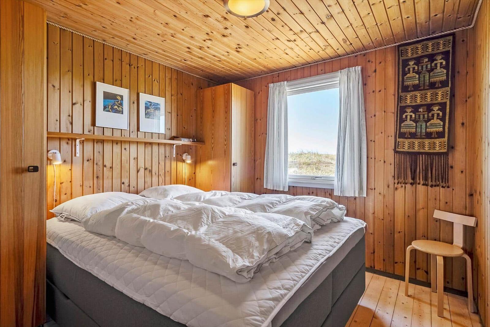 Schlafzimmer mit Holzwand, Bett, Fenster und Stuhl