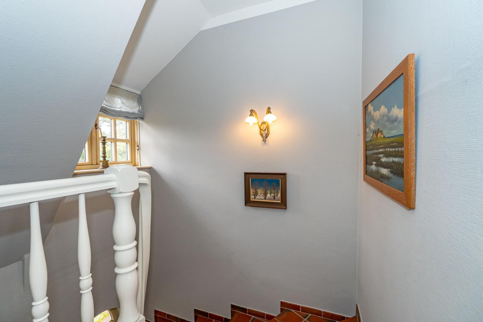 Hausflur mit Treppenhaus, Wandbeleuchtung und Bildern an der Wand.
