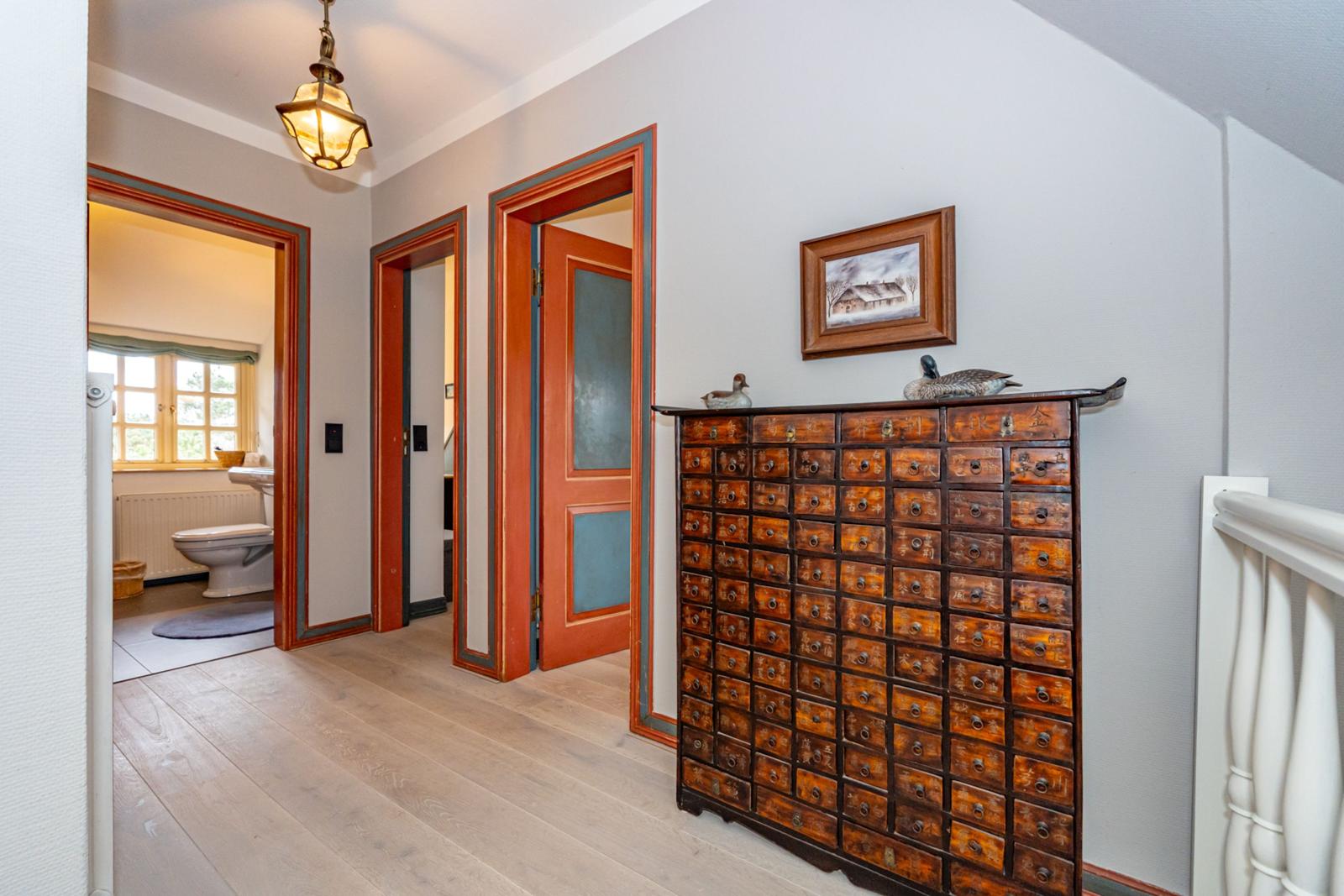 Flur mit Holzboden, roten Türen und antikem Schrank mit vielen Schubladen.