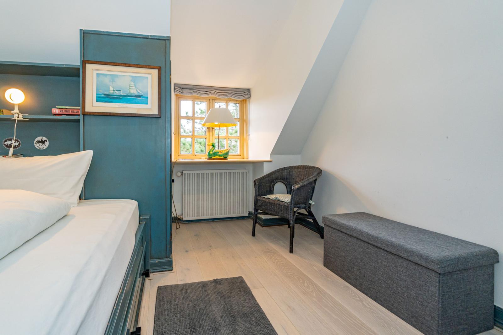 Schlafzimmer mit Bett, Stuhl und Fenster. Holzboden und Wand mit Bild.