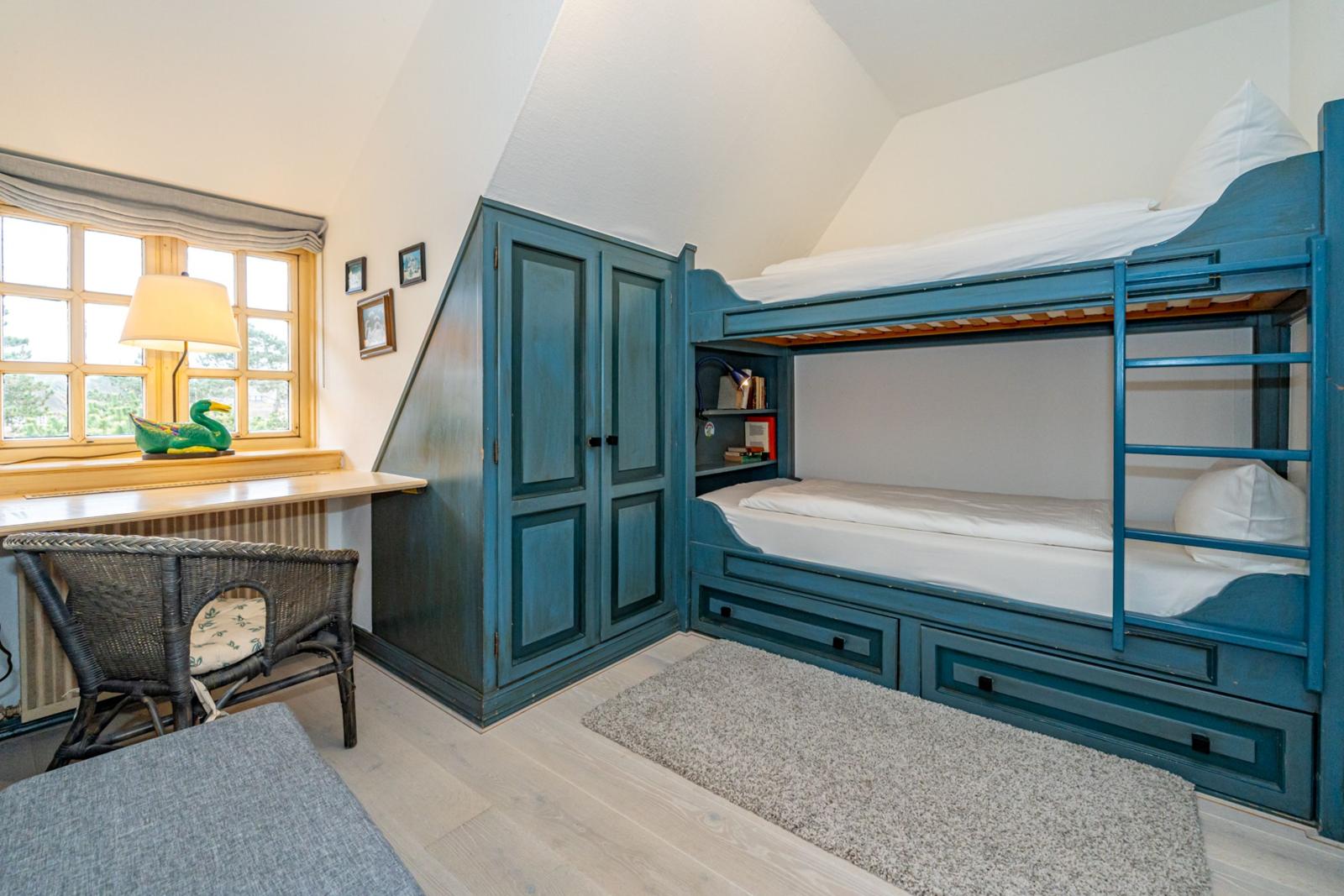 Schlafzimmer mit Doppelstockbett, Schrank und Fenster mit Sitzbank.