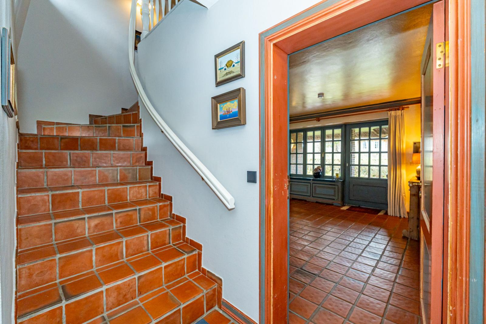 Treppe mit Terrakottastufen führt zu einem Raum mit Terrakottboden und Fenstern.