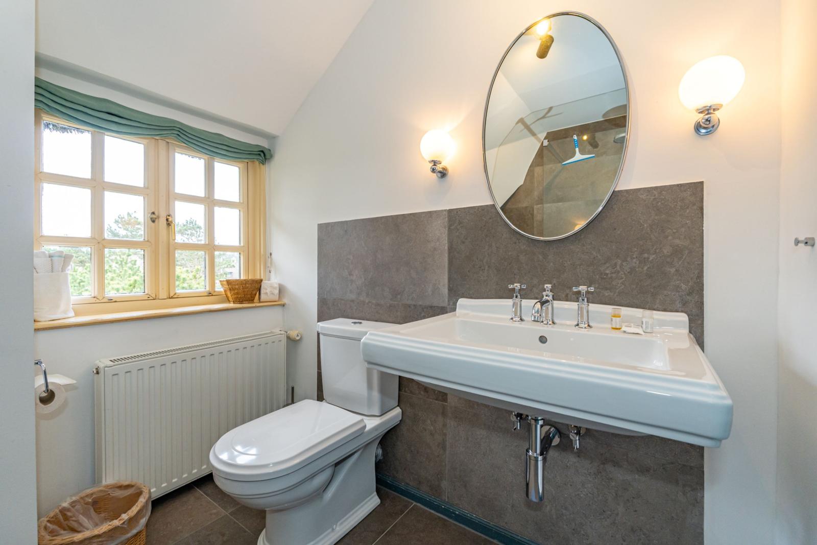 Badezimmer mit Toilette, Waschbecken und Fenster mit Blick auf Grün.