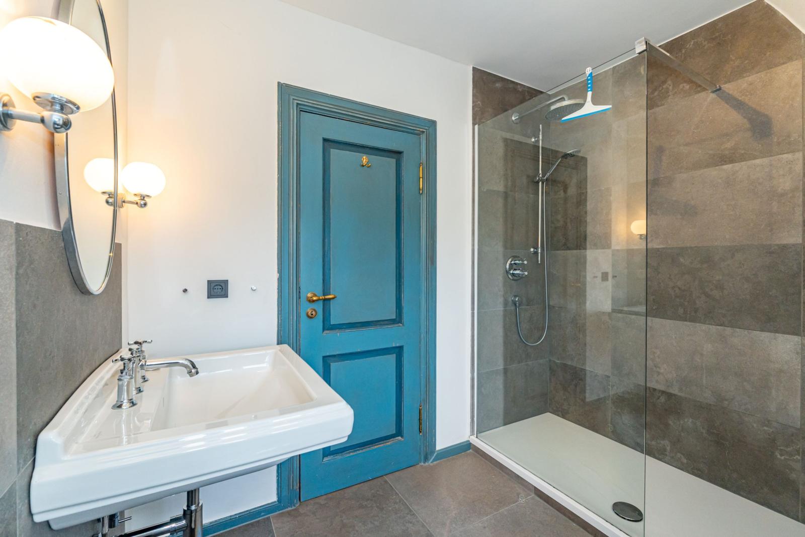 Badezimmer mit Dusche, Waschbecken und blauer Tür.