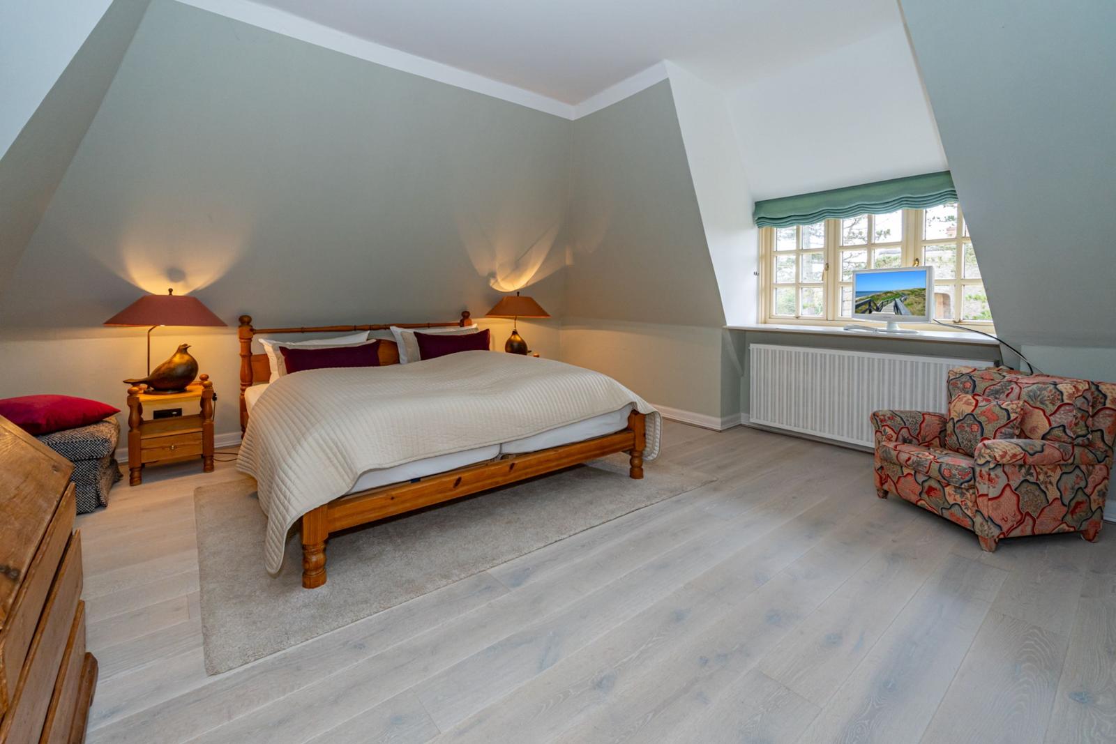 Schlafzimmer mit Dachschrägen, Bett, Nachttisch, Sessel und Fenster.