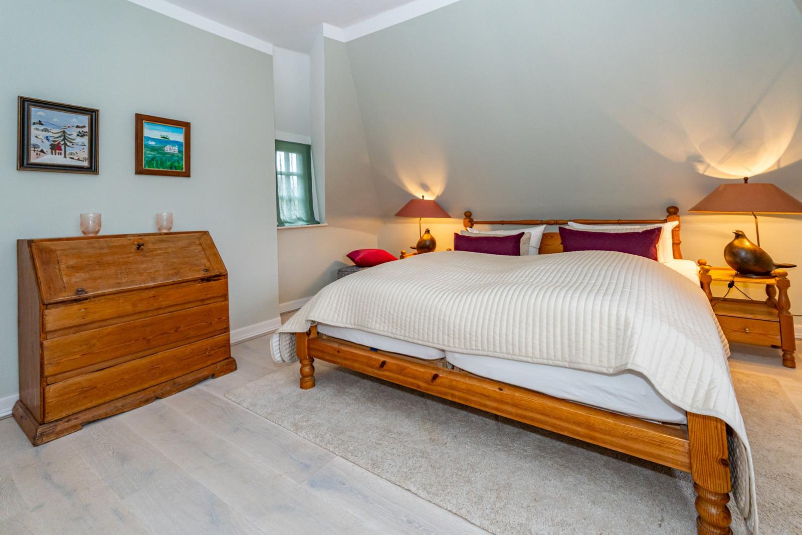 Schlafzimmer mit Holzbett, Nachttischen und Schrank. Wandbilder und Fenster sichtbar.