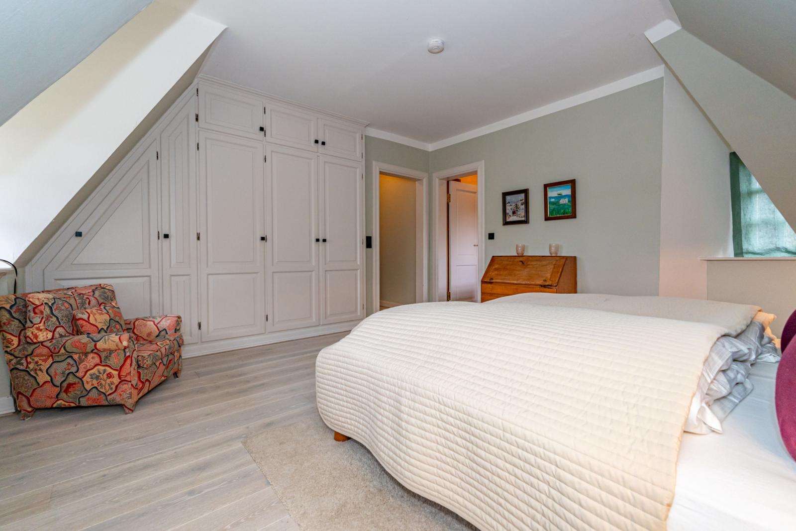 Schlafzimmer mit Dachschräge, Bett, Kleiderschrank und Sessel.