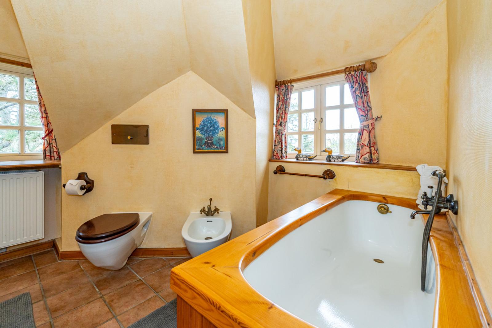 Bad mit Holzbadewanne, Toilette und Bidet unter schrägen Decken.