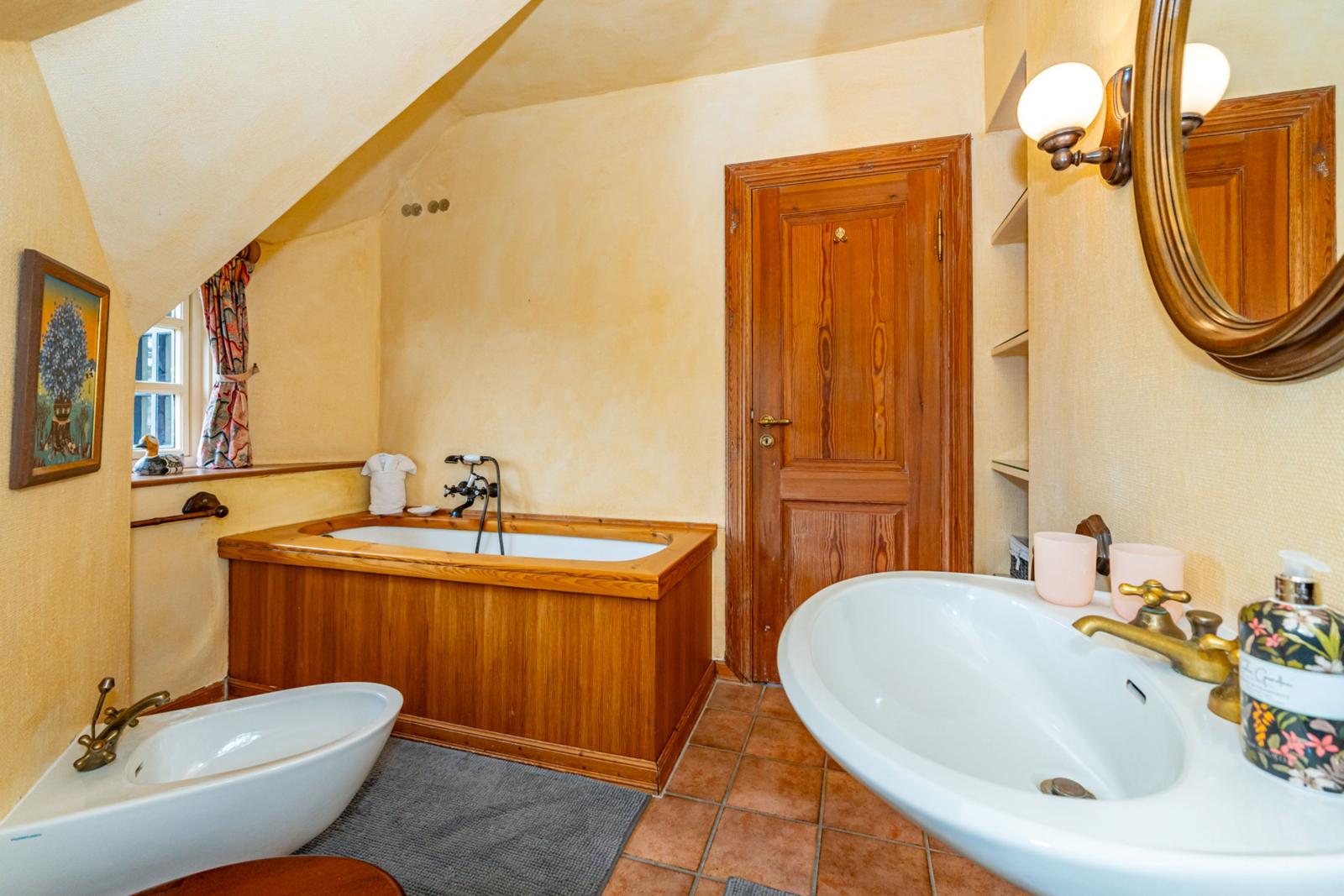 Badezimmer mit Holzbadewanne, Waschbecken und Spiegel