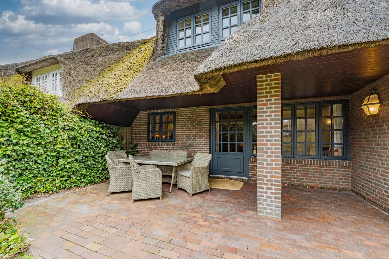 Haus mit Strohdach, Terrasse mit Sitzgruppe und grüner Hecke