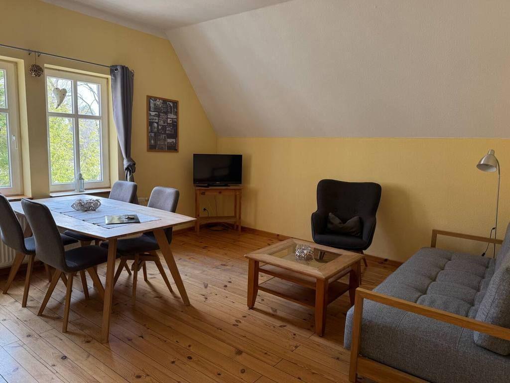 Wohn- und Essbereich mit Holzboden, Sofa, Sessel, Esstisch und TV.