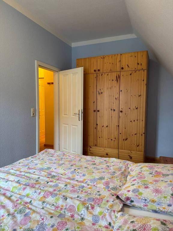 Schlafzimmer mit Holzschrank und Bett mit gemustertem Bettzeug. Tür führt in Bad.