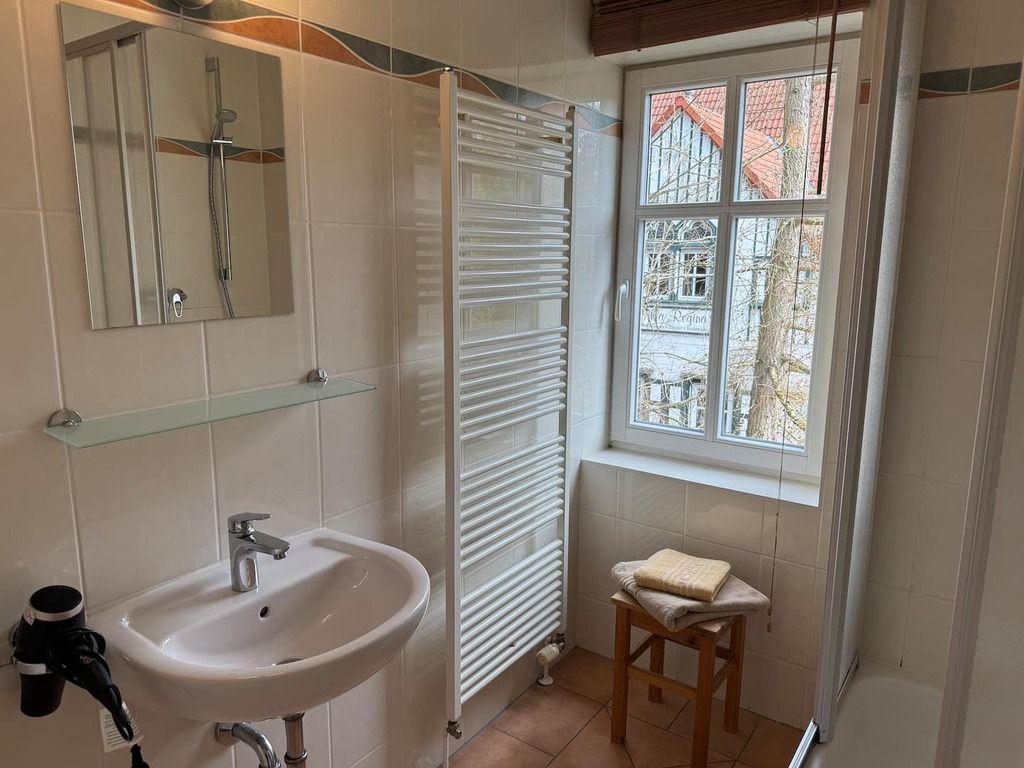 Badezimmer mit Waschbecken, Spiegel, Heizung und Fenster mit Blick nach außen.