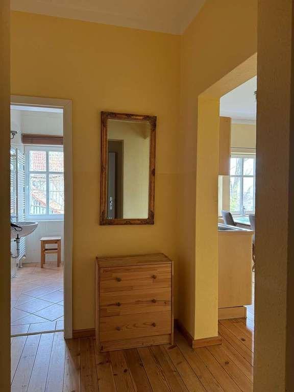 Hausflur mit Holzschrank, Spiegel und Blick in Bad und Küche.