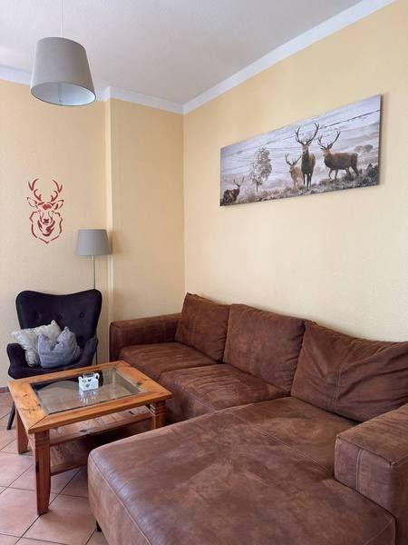 Wohnzimmer mit braunem Sofa, Glas-Tisch und Wandbild mit Hirschen.