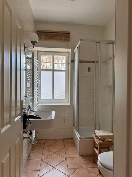 Badezimmer mit Dusche, Waschbecken und Toilette. Fenster mit Holzjalousie.