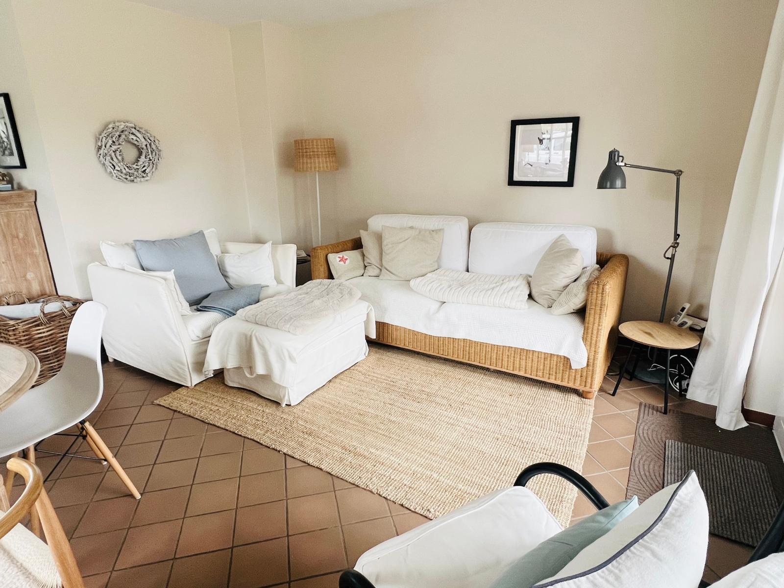 Wohnzimmer mit Sofa, Sessel und Teppich auf Fliesenboden.