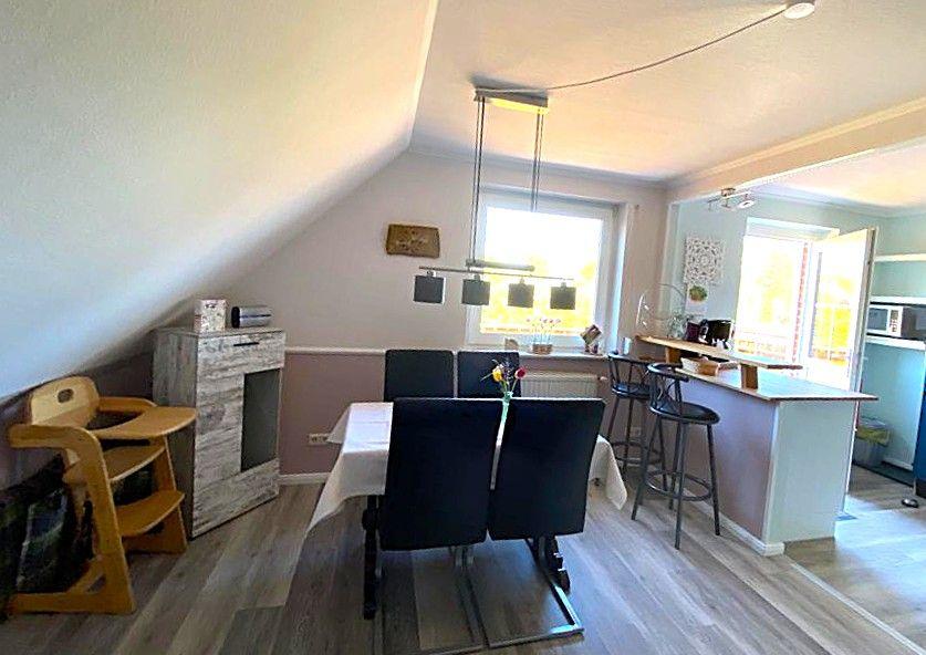 Esszimmer mit Tisch, Stühlen und Küchenbereich im Hintergrund.