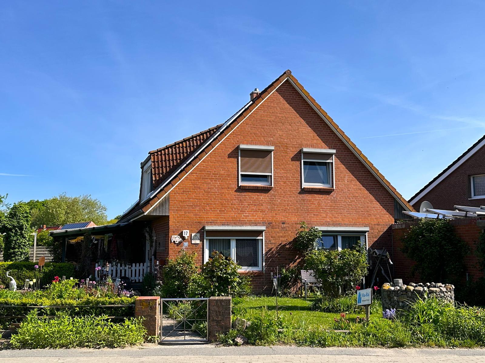 Rotes Backsteinhaus mit Garten und Terrasse unter blauem Himmel.