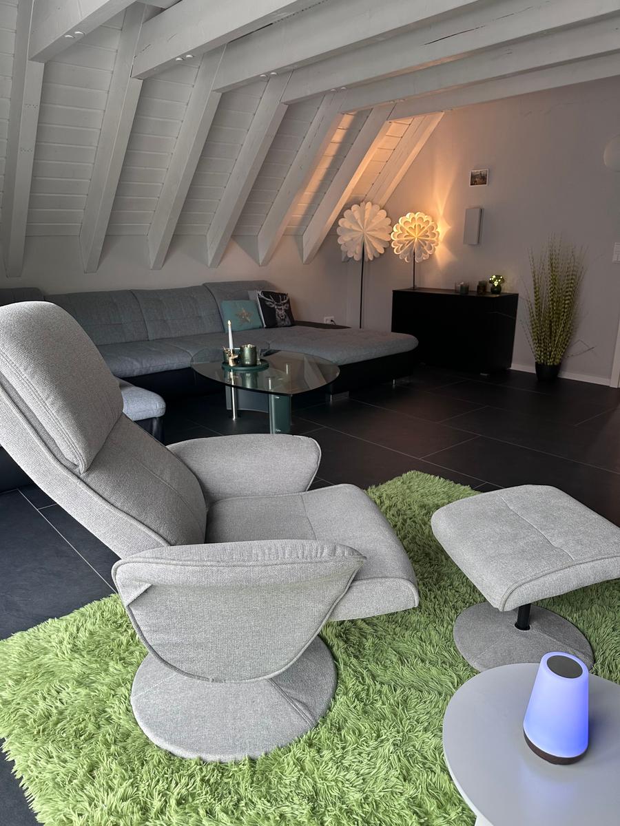 Ein Wohnzimmer mit grauem Sofa, modernem Sessel und grünem Teppich unter der Dachschräge.