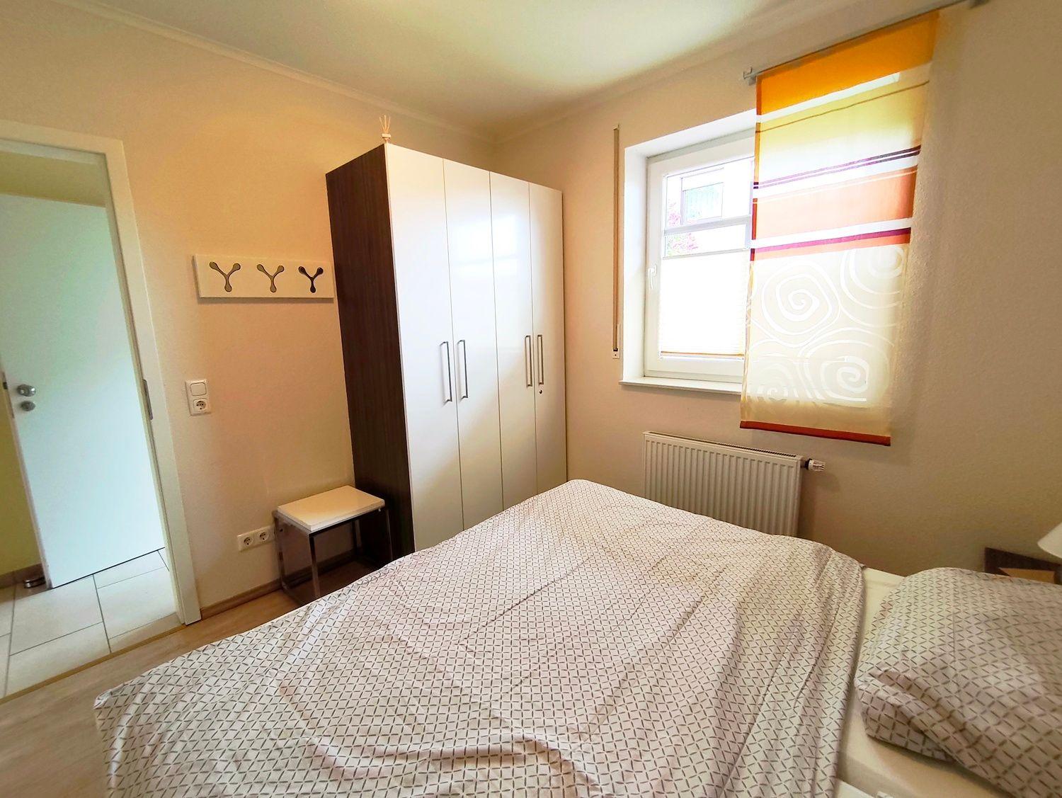 Schlafzimmer mit Bett, Kleiderschrank und Fenster mit Rollladen.