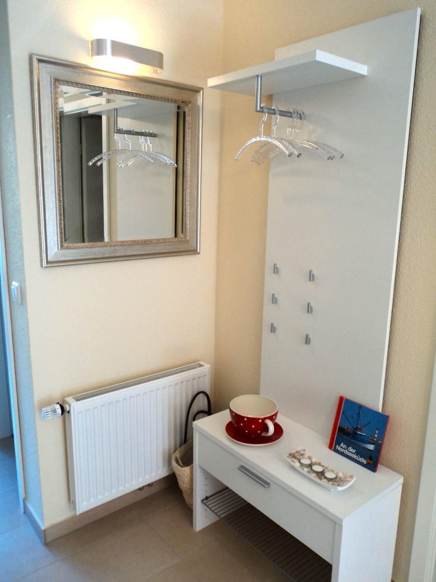 Eingangsbereich mit Spiegel, Garderobe und kleinem Tisch mit Tasse und Buch.