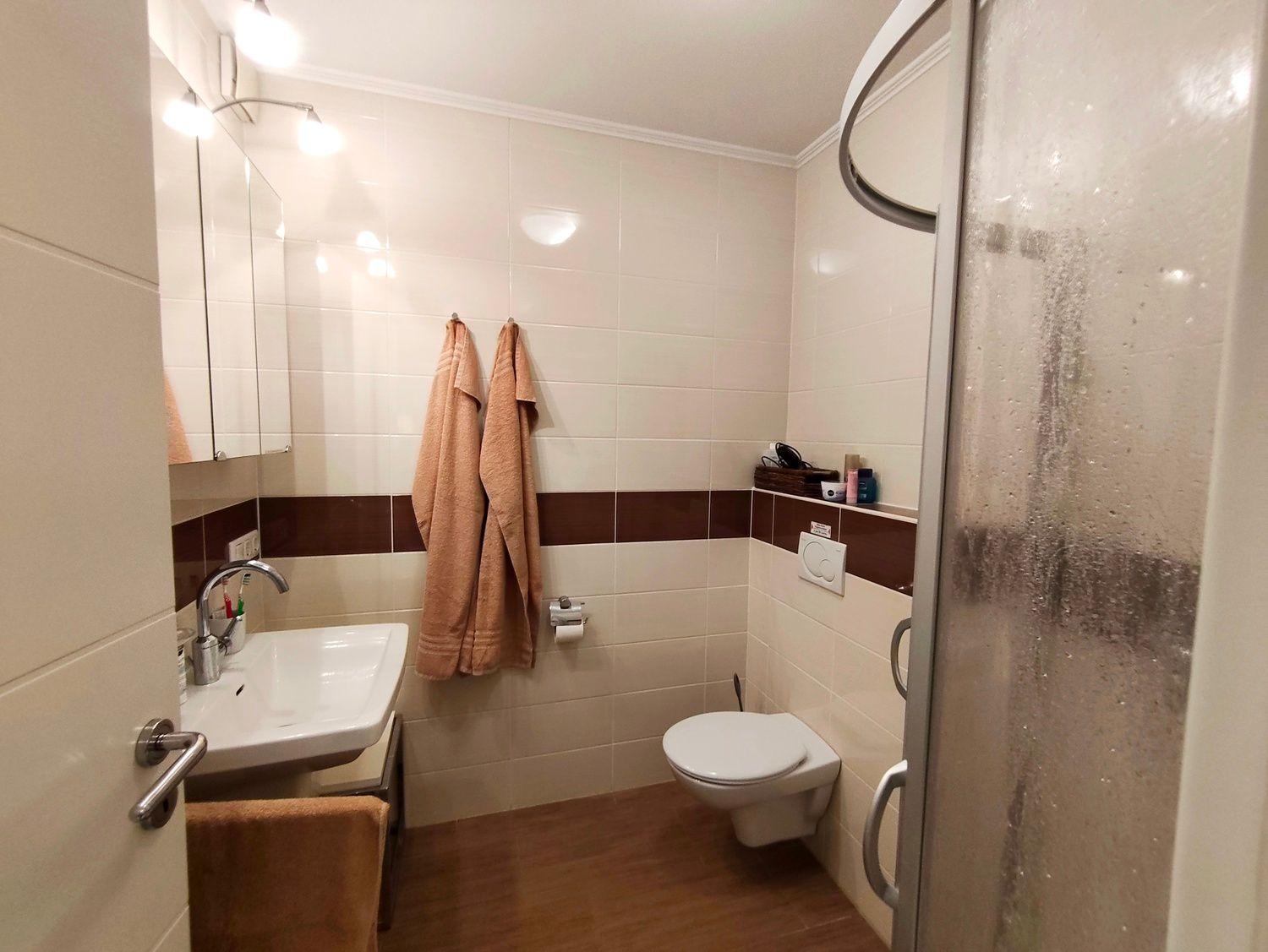 Badezimmer mit Dusche, Toilette und Waschbecken. Braune Handtücher hängen an der Wand.