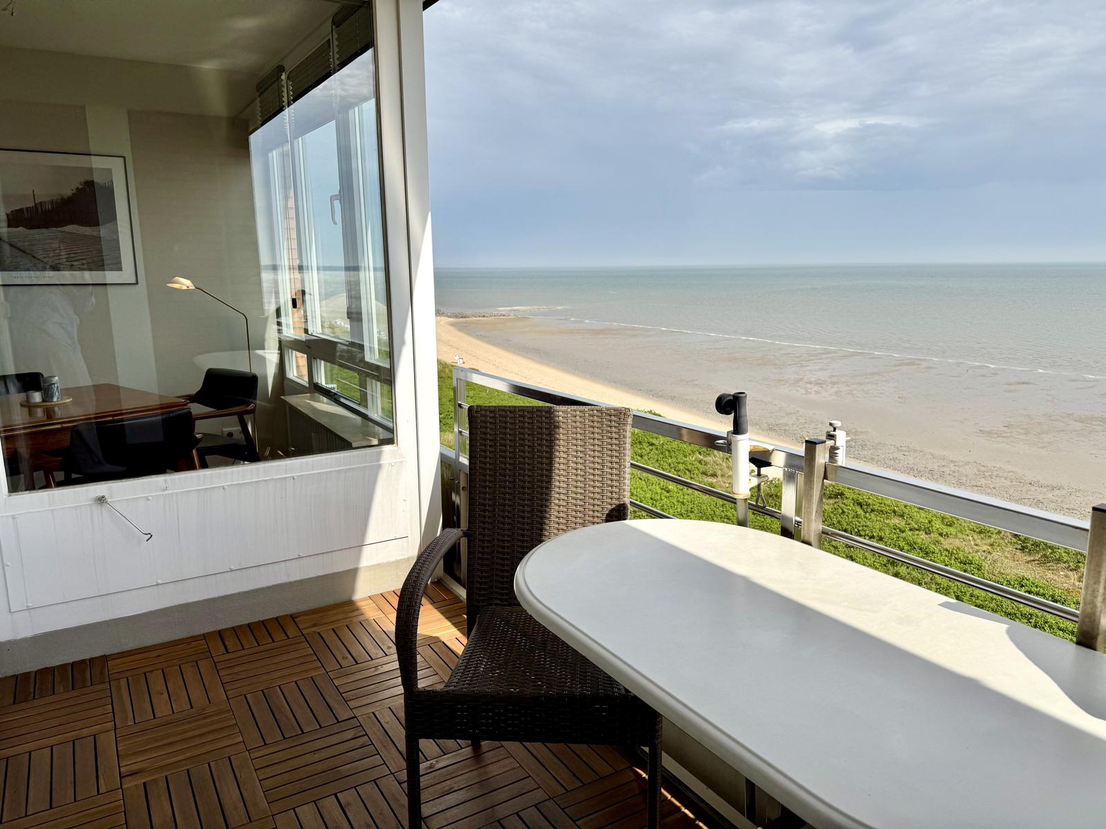 Terrasse mit Tisch und Stühlen. Blick auf Strand und Meer.