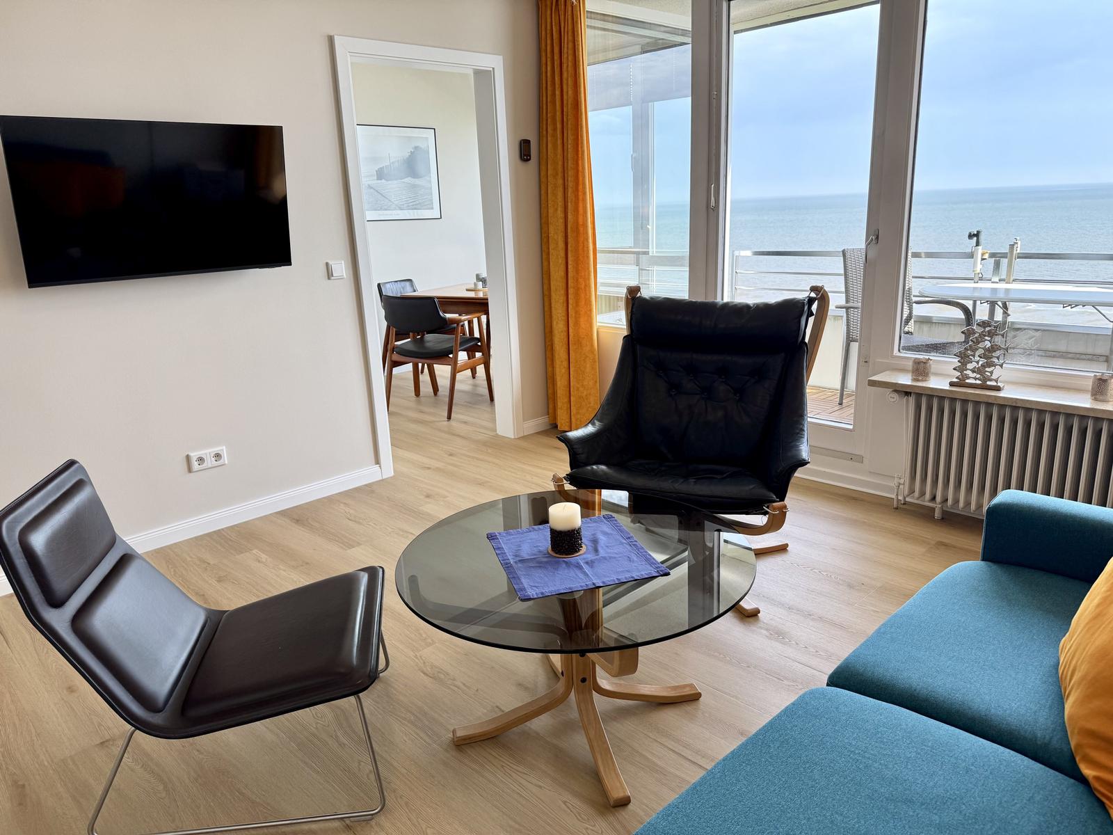 Wohnzimmer mit Sofa, Sessel und Blick aufs Meer