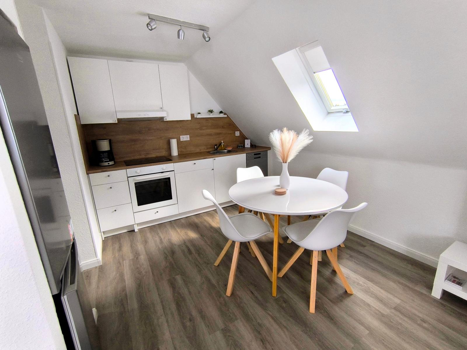 Küche mit Essbereich unter Dachschrägen, weißer Tisch, vier Stühle, Dachfenster.