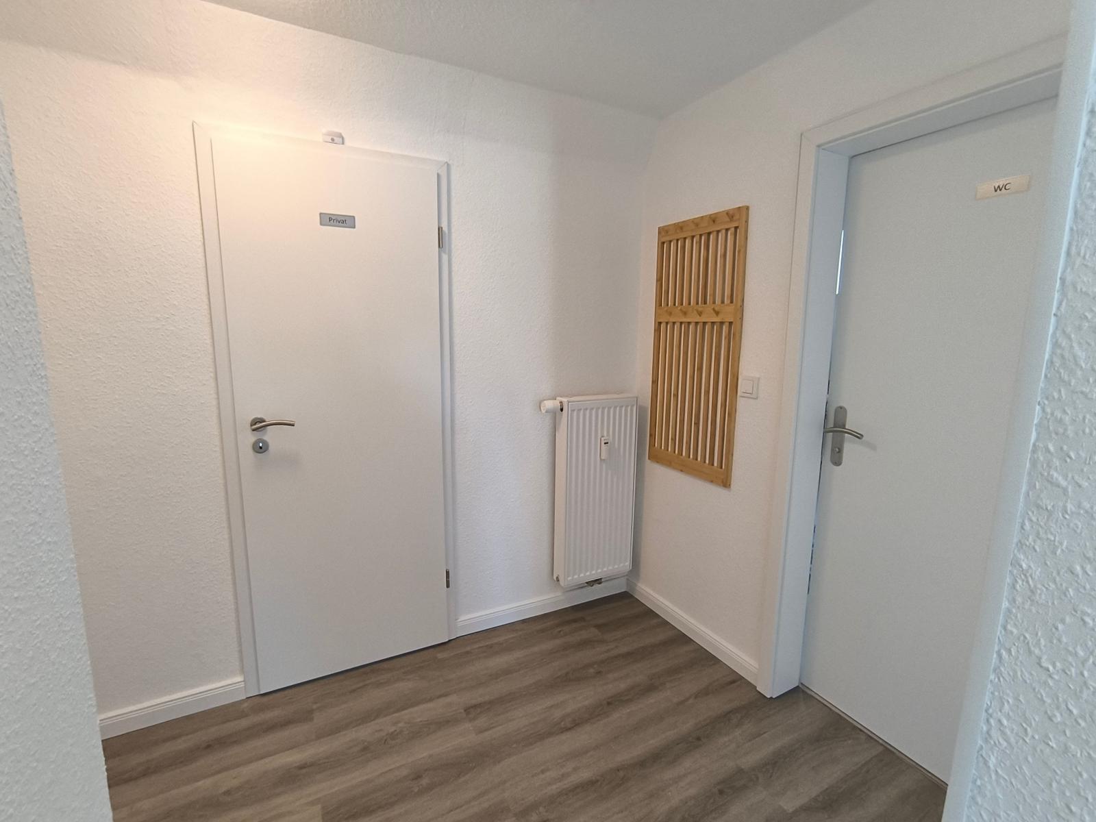 Flur mit Tür zu privatem Raum und WC, Holzpaneel an Wand, Heizkörper und Holzdielenboden.