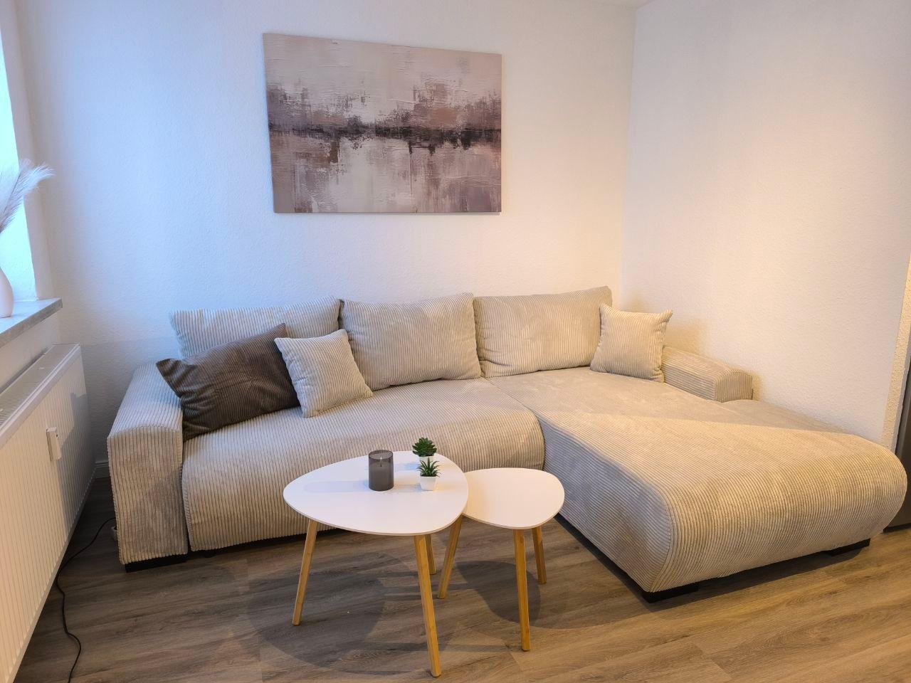 Ein Wohnzimmer mit Ecksofa, zwei runden Tischen und Wandbild.
