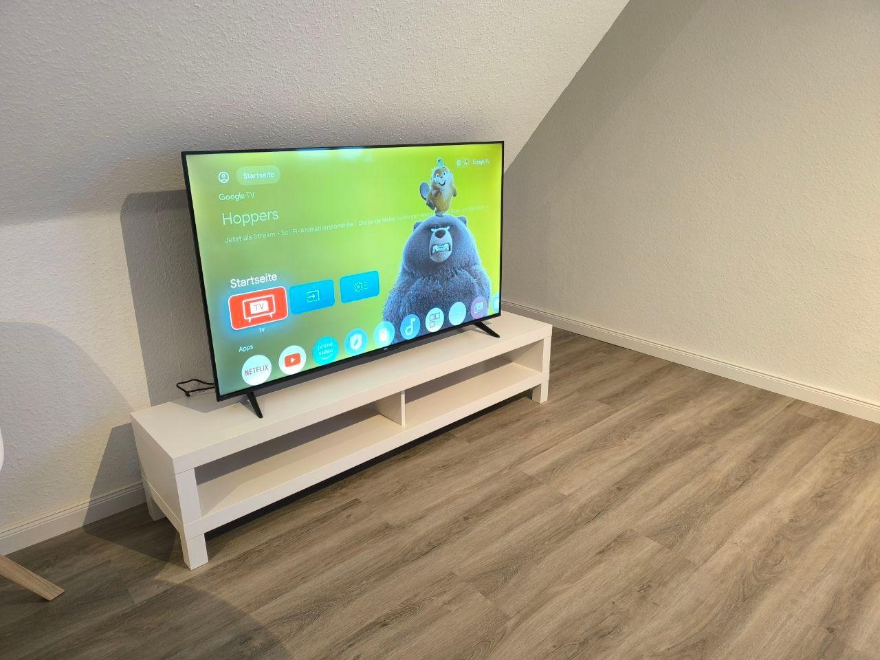 Fernseher auf weißem TV-Board in einem Raum mit Holzdielen und schräger Decke.