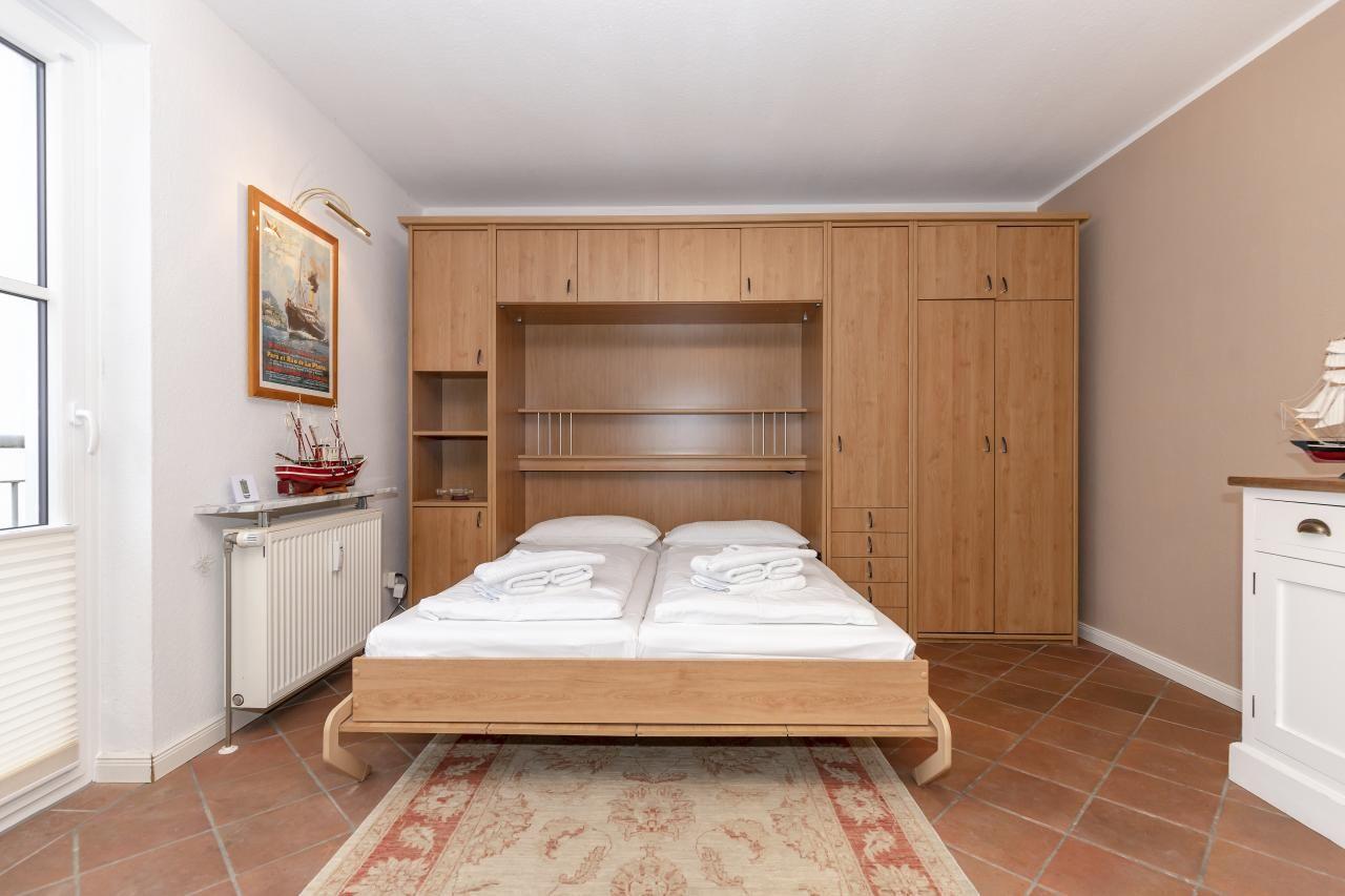 Schlafzimmer mit Doppelbett, Holzmöbel und Fenster. Teppich und Wandbild sichtbar.