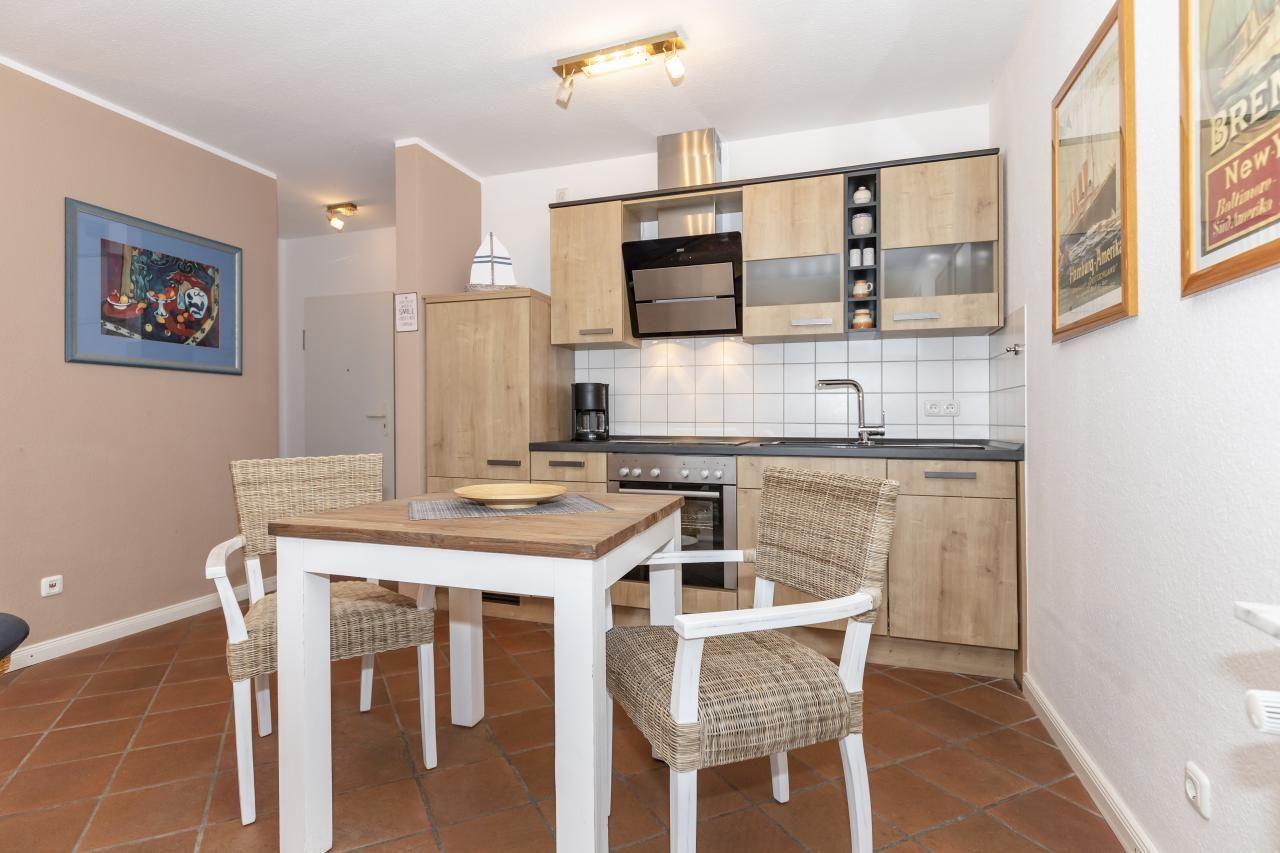 Küche mit Essbereich, Holzschränke, Tisch mit Stühlen und Wandbildern.