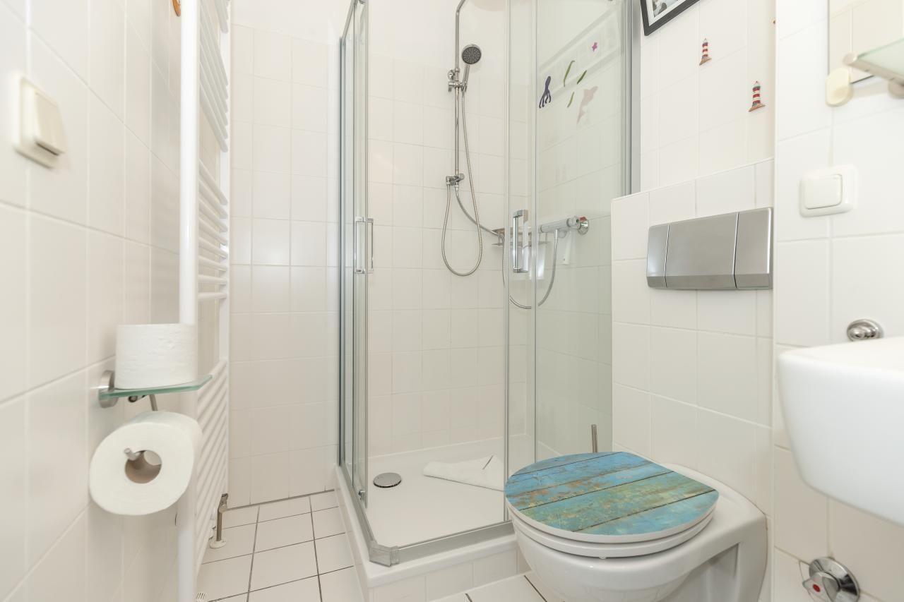 Badezimmer mit Dusche, Toilette und Waschbecken. Toilettenkorb hat blauen Holzdeckel.