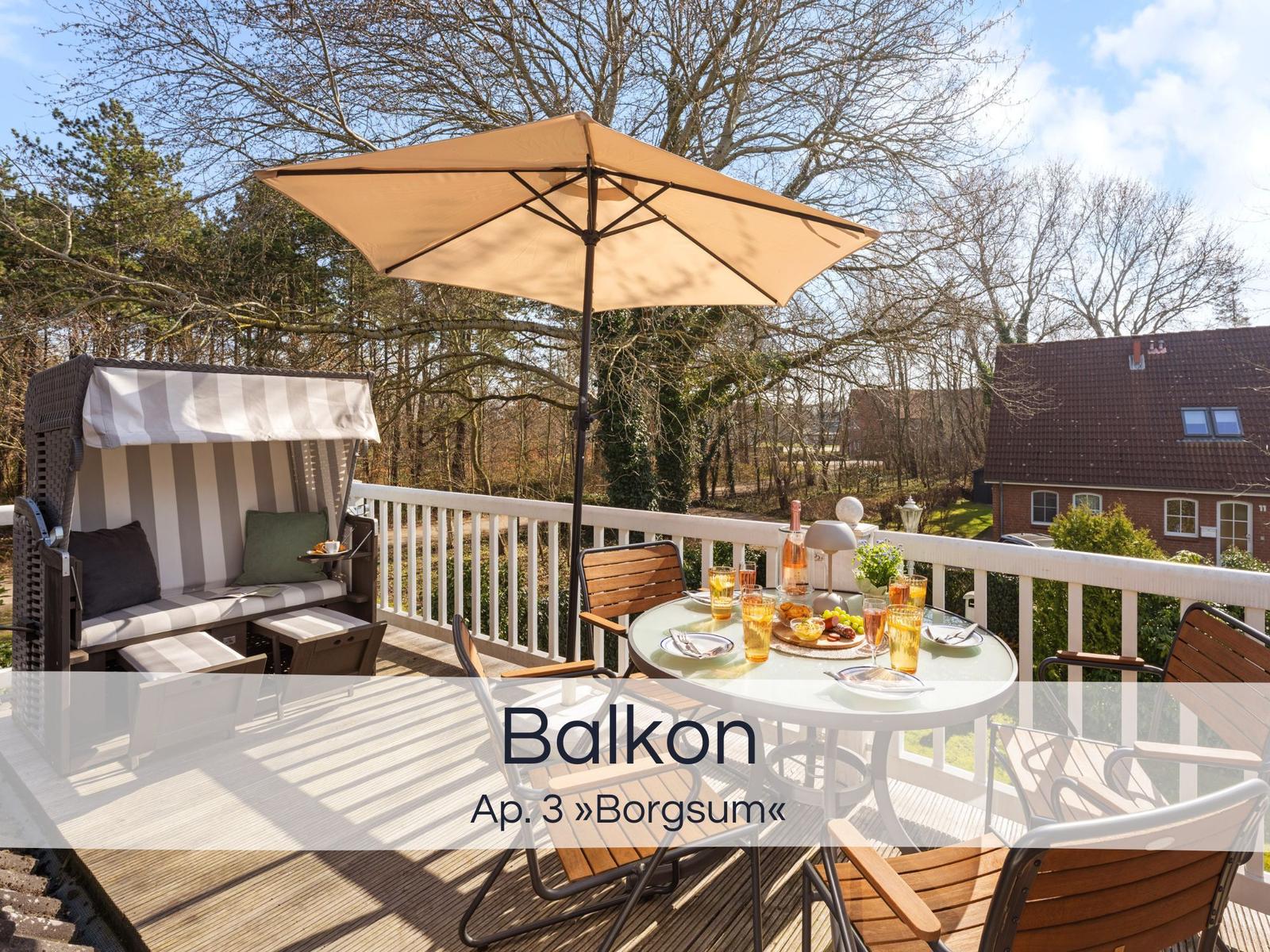 Terrasse mit Sonnenschirm, Esstisch und Liege. Blick auf Wald und Haus.